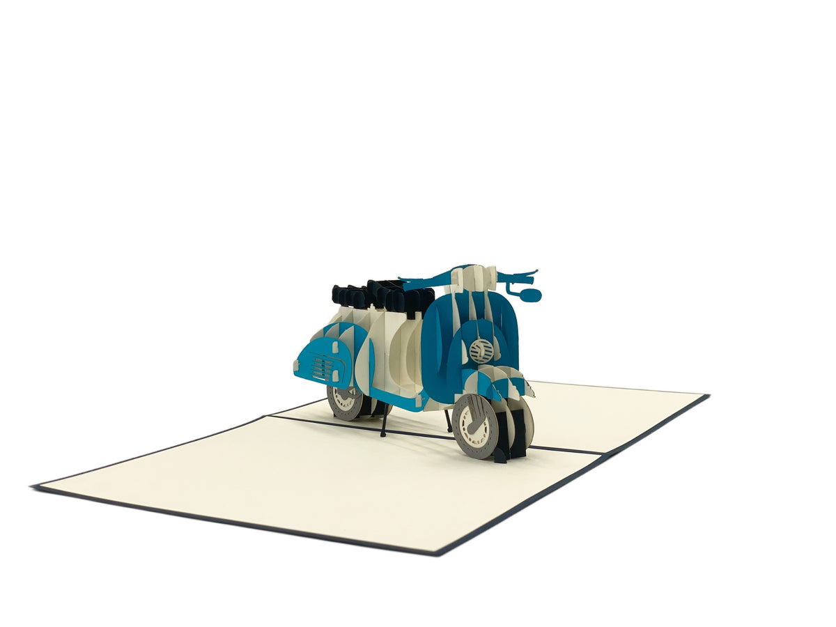 Aufgeklappte Pop-up-Karte mit einer blauen Vespa aus Papier, seitlich fotografiert.