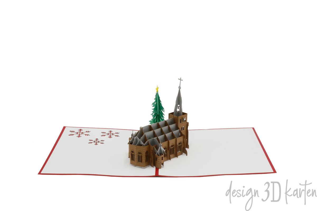 Aufgeklappte Pop-up-Karte mit Kirche und Tannenbaum aus Papier, schräg von der Seite fotografiert.