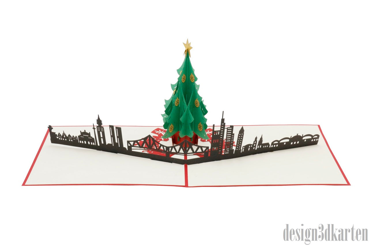 Aufgeklappte Pop-up-Karte mit Weihnachtsbaum vor der Frankfurter Skyline, schräg von der Seite fotografiert.