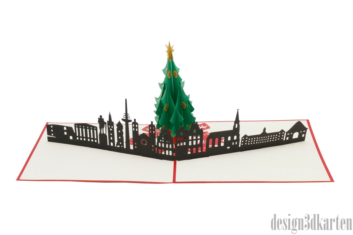 Aufgeklappte Pop-up-Karte mit Weihnachtsbaum vor der Münsteraner Skyline, seitlich fotografiert.