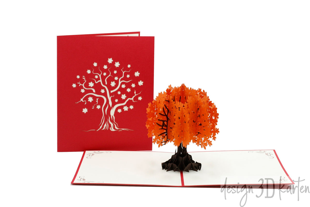 Aufgeklappte Pop-up-Karte mit einem orangefarbenen Herbstbaum, daneben die rote Kartenvorderseite mit Baum-Scherenschnitt.