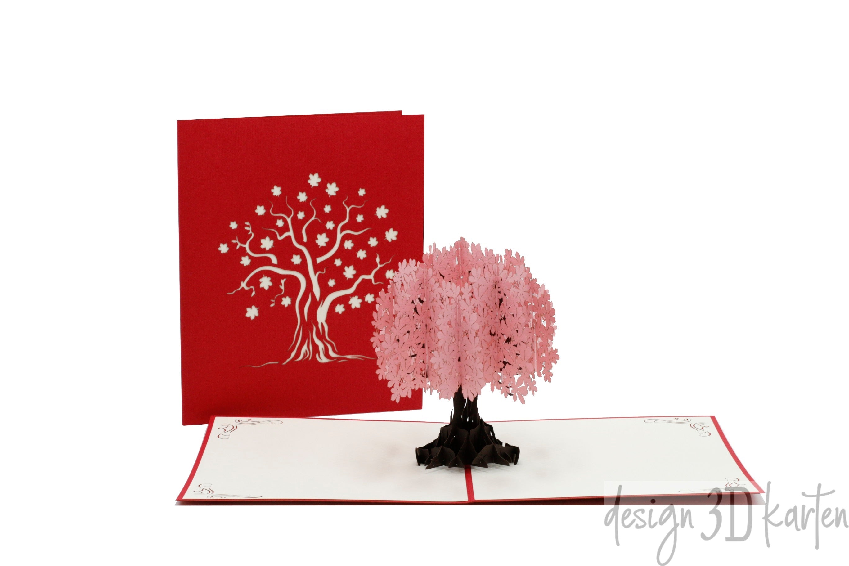 Aufgeklappte Pop-up-Karte mit einem rosa Blütenbaum, daneben die rote Kartenvorderseite mit Baum-Scherenschnitt.