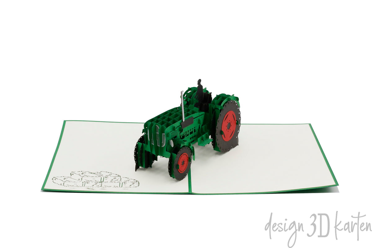 Aufgeklappte Pop-up-Karte mit grünem Oldtimer-Traktor aus Papier, seitlich fotografiert.